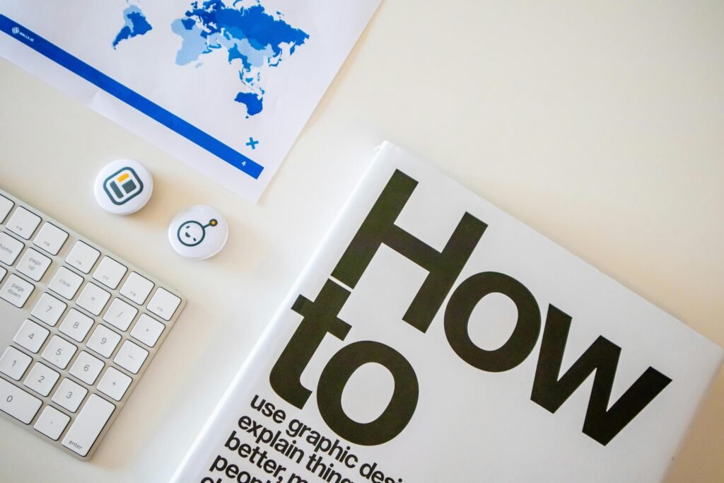 Stylish desk setup with a how-to book, keyboard, and world map on paper.